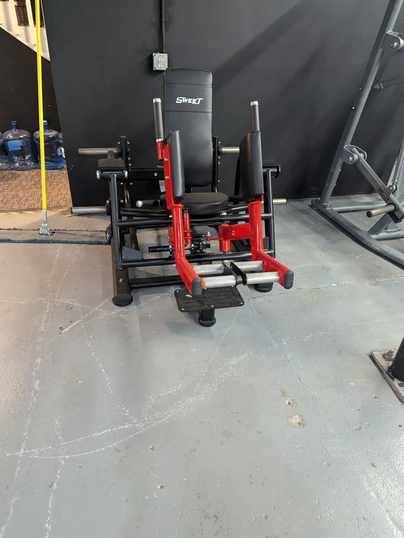 Plate loaded Sweet Glute and Outer Thigh machine in black, red, and silver by Muscle D Fitness, showing the seat and leg pads.