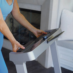 WalkingPad Denise Austin 2.0 foldable treadmill with a woman adjusting settings on a blue treadmill in a home gym scene.