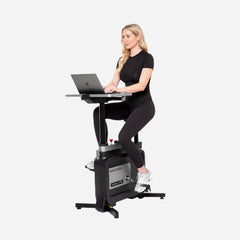 Woman using WalkingPad foldable exercise bike while working on her laptop at a desk, demonstrating a compact under-desk fitness solution.
